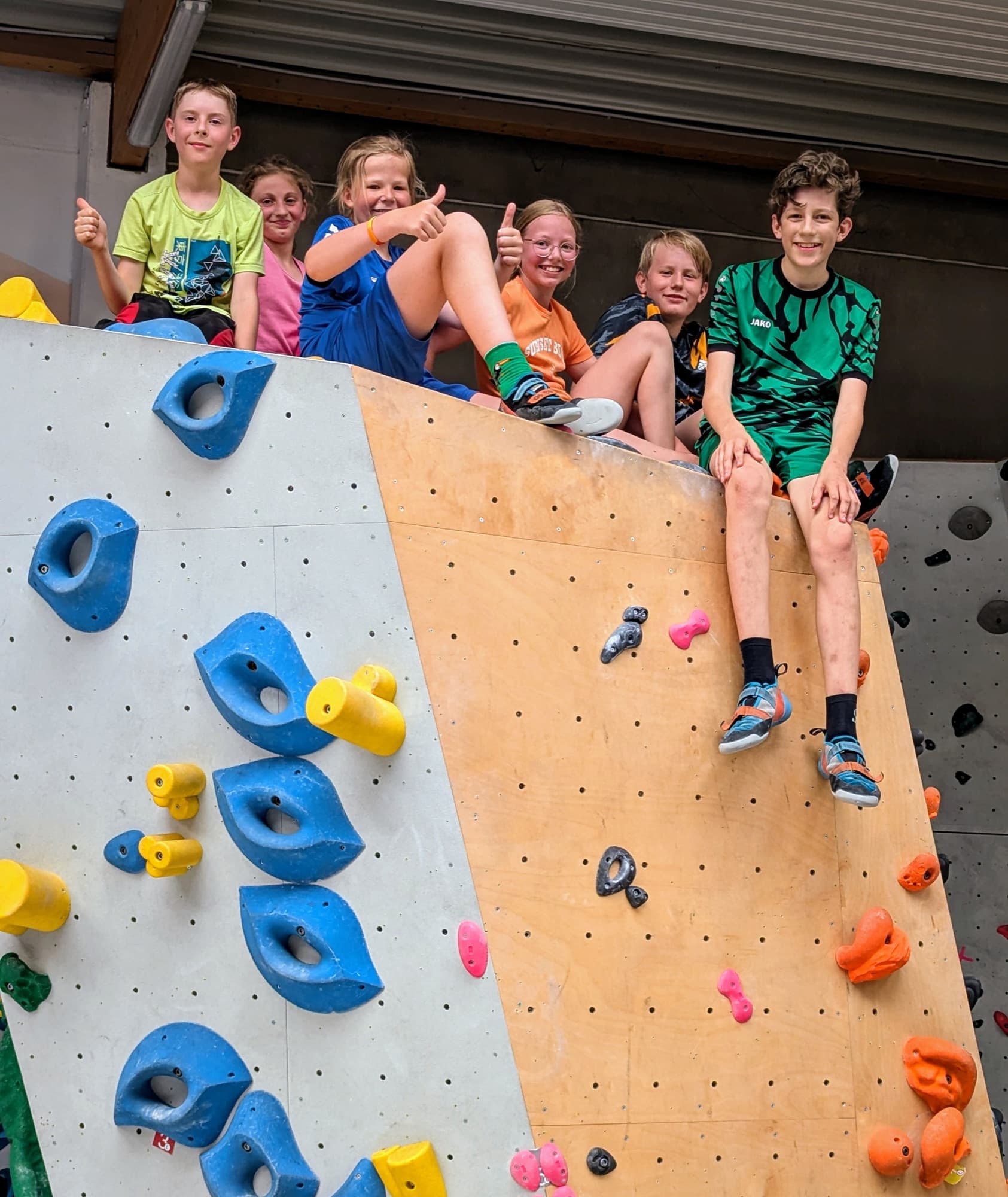 Eine Gruppe Kinder sitzt stolz oben auf der Boulderwand.