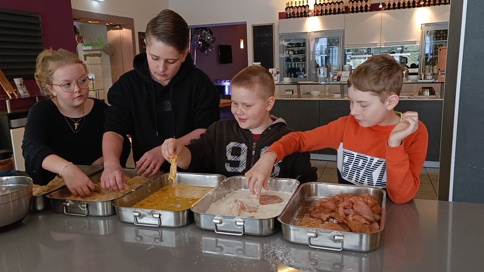 Kinder panieren gemeinsam Schnitzel im Kochkurs.