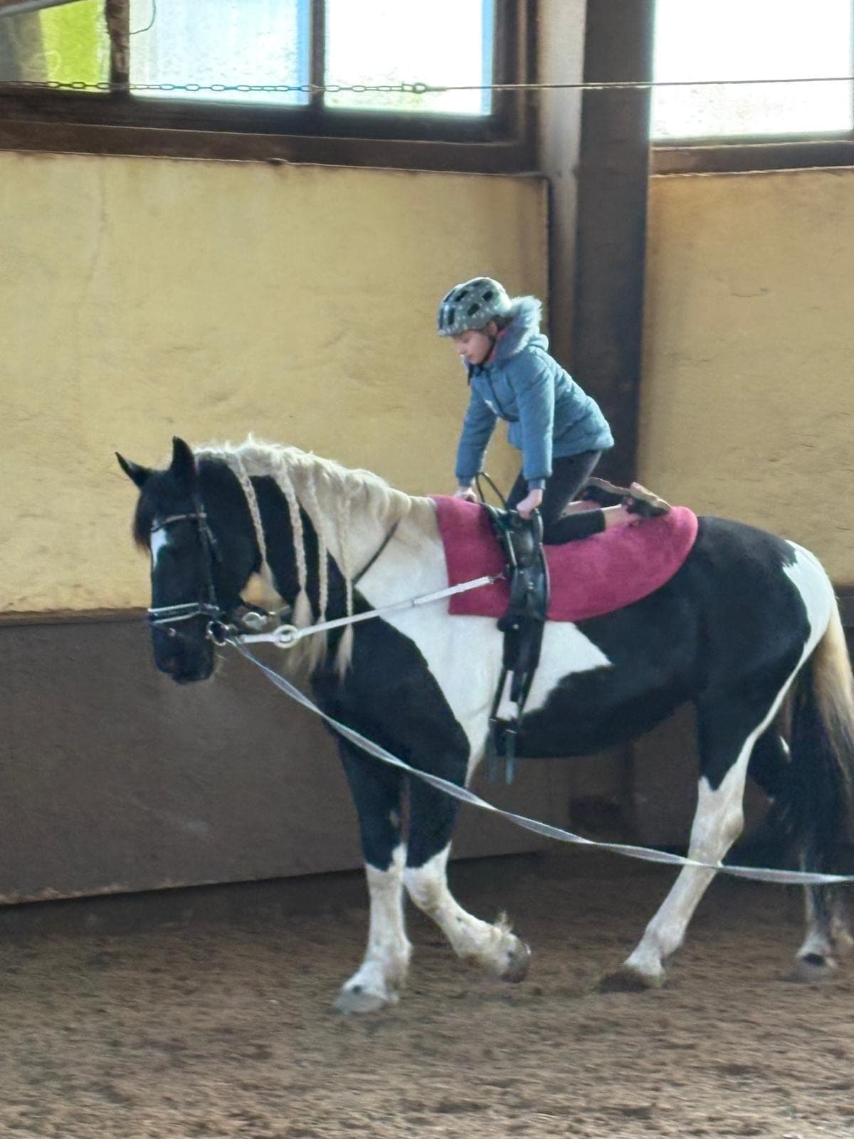 Ein Kind übt bei der Reitpädagogik kniend das Gleichgewicht auf dem Pferderücken.