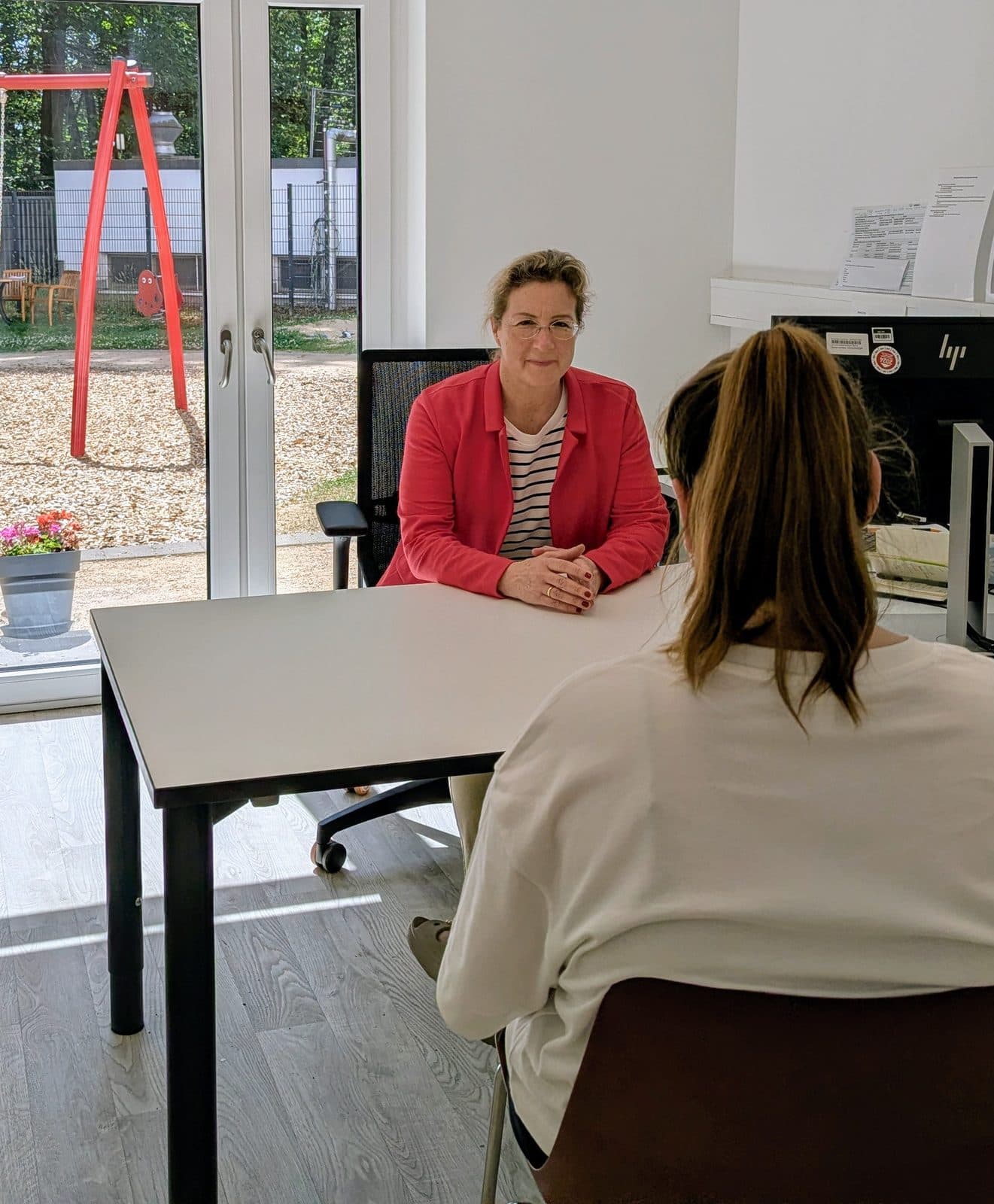 Ärztin im Beratungsgespräch mit einer jungen Frau an einem Tisch im hellen Sprechzimmer des Langzeitnachsorgezentrums