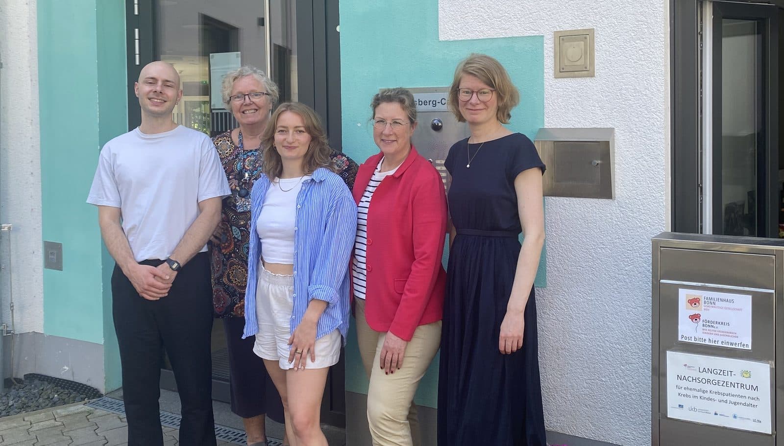 Das fünfköpfige Team der Langzeitnachsorge vor dem Eingang des FAMILIENHAUSES, neben dem Schild „Langzeitnachsorgezentrum“