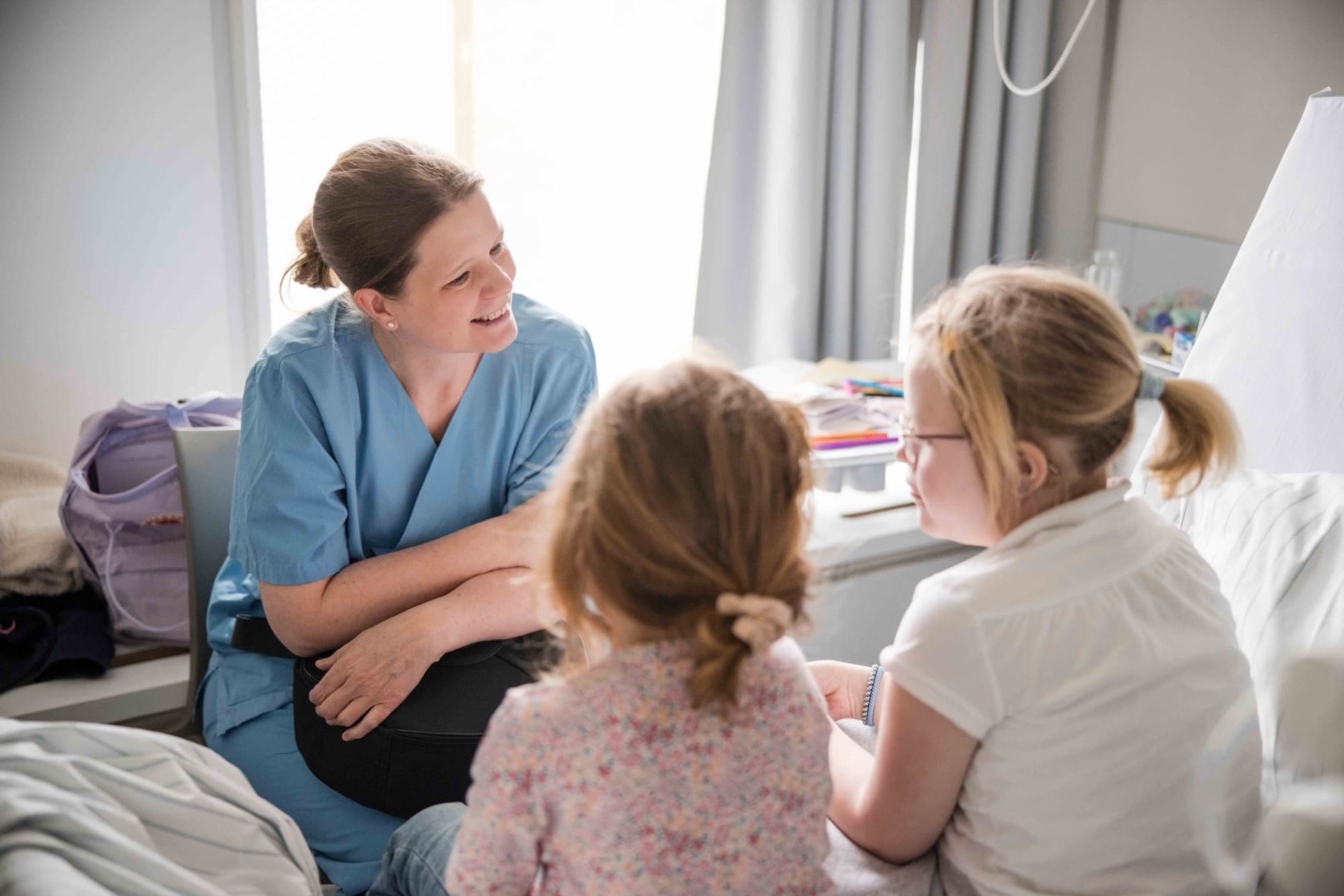 Eine Musiktherapeutin im Austausch mit zwei Kindern am Bett.