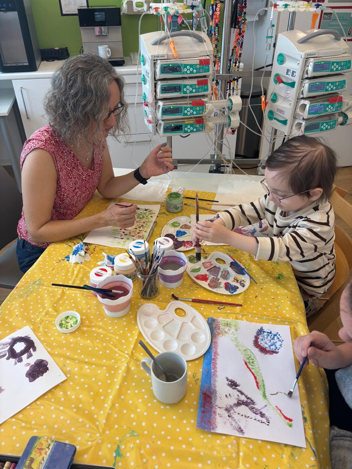 Kunsttherapeutin und Kind malen gemeinsam an einem Tisch auf der kinderonkologischen Station